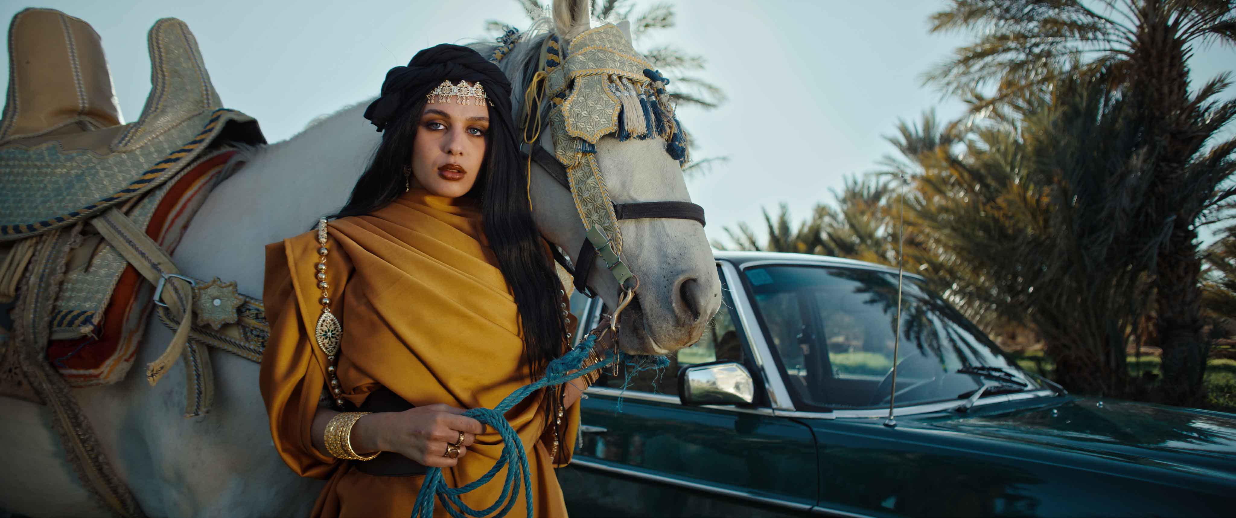 Close-up of a Moroccan woman with blue eyes in traditional jewelry beside a white decorated horse