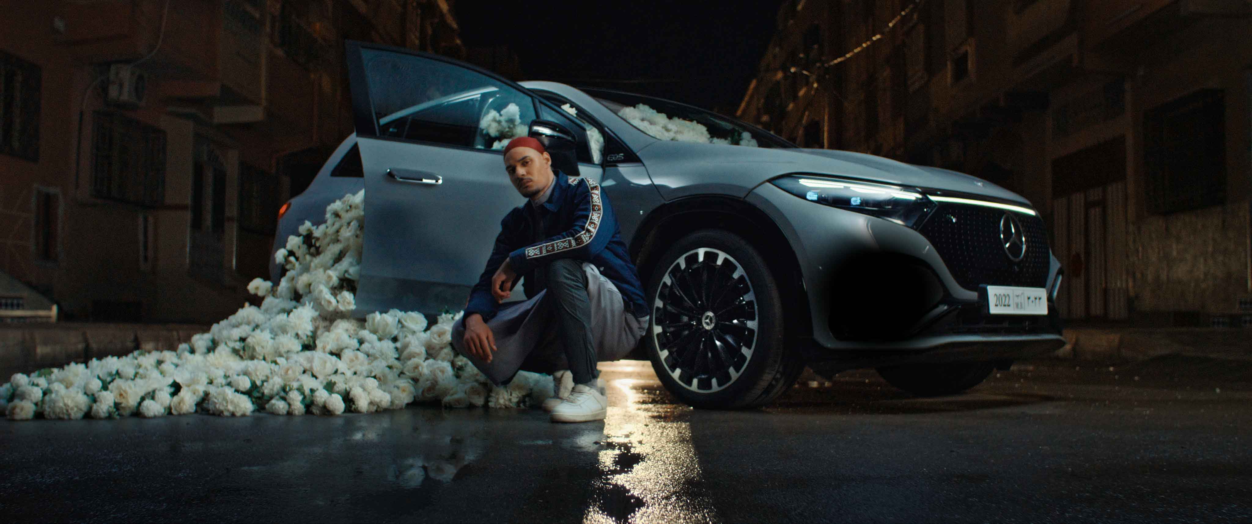Rapper crouching by Mercedes EQS with white flowers in Moroccan street